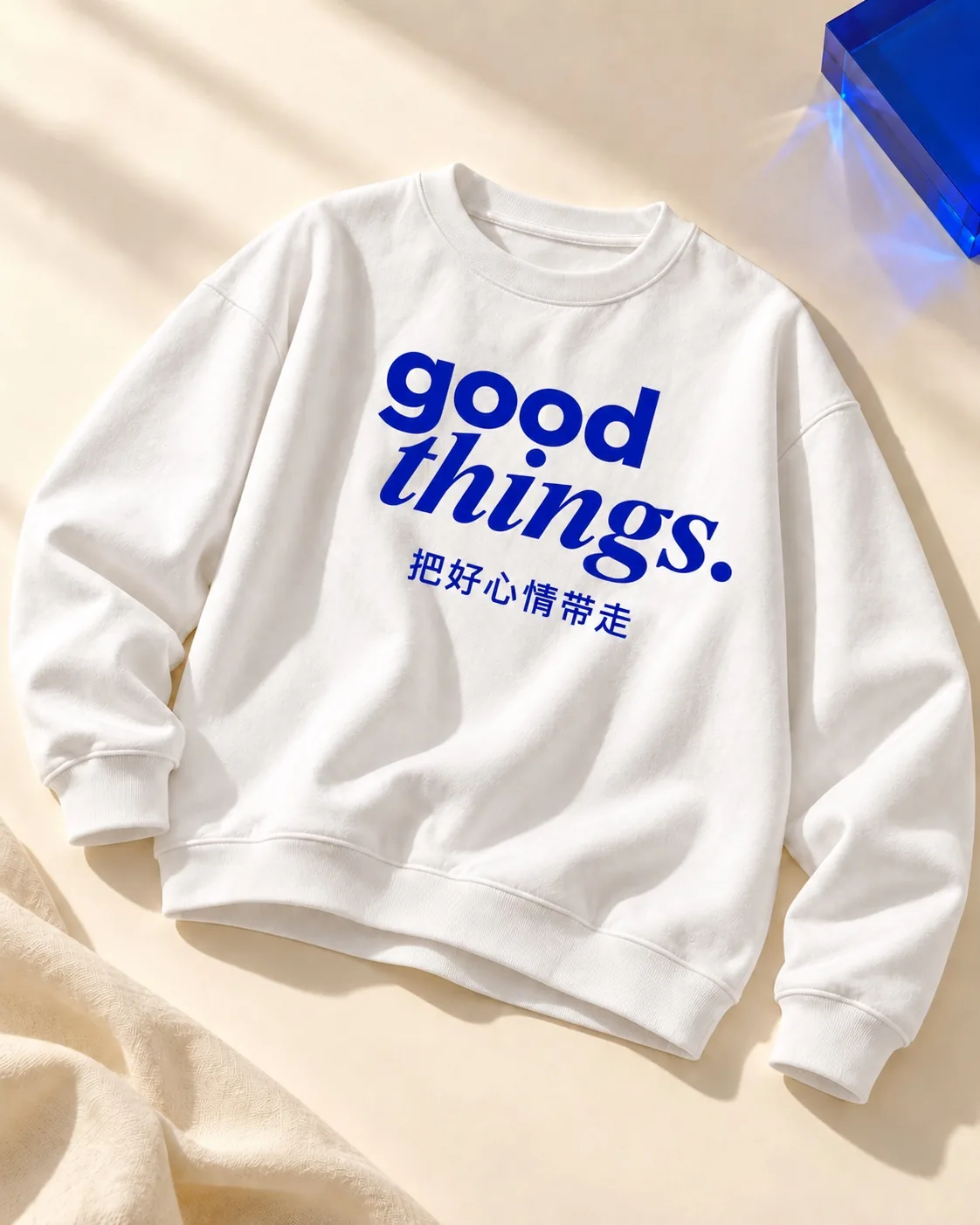 暖奶油背景与蓝色亚克力旁的白卫衣，印有蓝色good things和把好心情带走