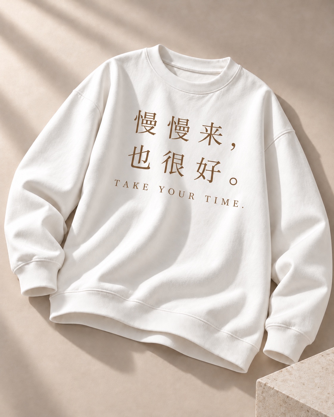 暖砂色摄影背景中的奶白卫衣，印有棕色慢慢来也很好文字